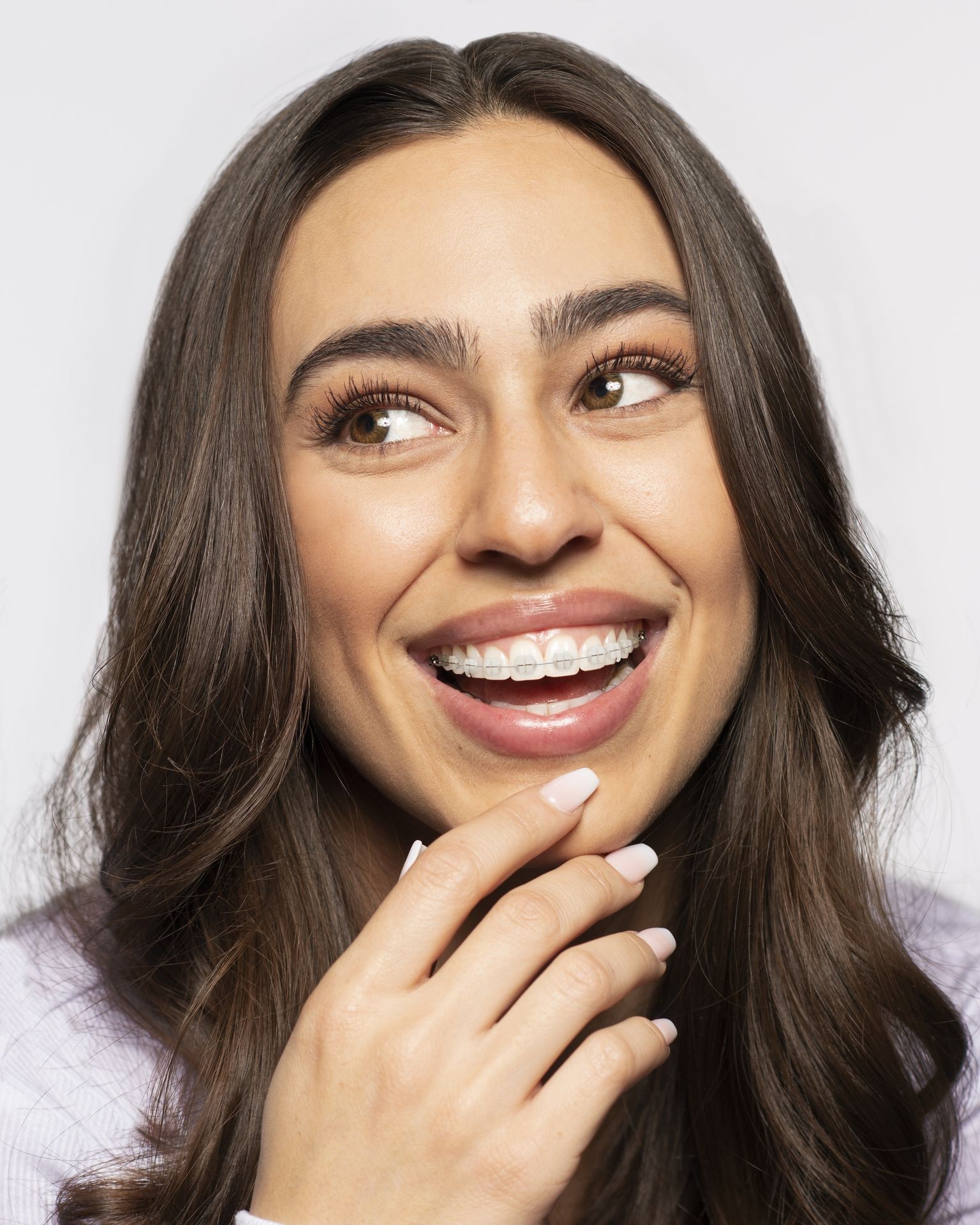 A woman smiling and showing her LightForce clear, custom braces for orthodontic treatment.